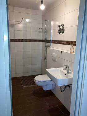 Weißgefliestes Badezimmer mit Dusche und Glastrennwand. Der Boden ist mit dunkelbraunen Bodenplatten verlegt das sich im Mosaik stiel als Bordüre an der Wand wiederfindet. - 3 Zimmer Etagenwohnung in Mannheim