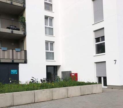 Eingangsbereich des Hauses mit weißer Fassade, Balkonen und gepflegter Grünfläche - 