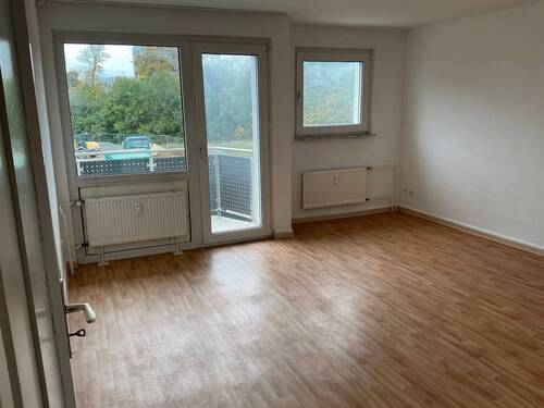 Wohnzimmer mit Bodenbelag in Holzoptik, Wände weiß tapeziert, Zugang zum Balkon - 