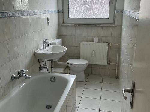 Badezimmer mit Badewanne und hellen Wand- und Bodenfliesen - 