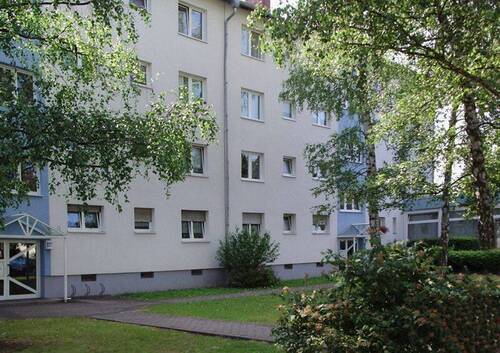Außenansicht eines mehrstöckigen Wohngebäudes, umgeben von Bäumen und Sträuchern. - Schöne 3,5-Zimmer-Wohnung mit Balkon zu vermieten!
