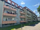 Rückansicht des mehrstöckigen Wohngebäudes mit Balkonen, umgeben von Grünanlagen mit Bäumen und grünen Sträuchern - Wir modernisieren für Sie diese gemütliche Wohnung in ruhiger Lage!