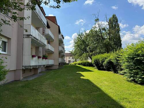 Rückansicht des mehrstöckigen Wohngebäudes mit Balkonen, umgeben von Grünanlagen mit Bäumen und grünen Sträuchern - Etagenwohnung mit 64,60 m&sup2; in Bad Vilbel zur Miete