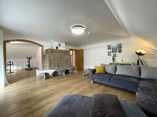 Dachgeschoss: Wohnzimmer mit gemütlichem Kachelofen und weiter in den Fitnessraum - 