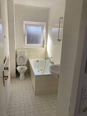 Bad mit Badewanne, weißen Sanitärobjekten, hellgelbem Fliesenspiegel und weiß-grauen Bodenfliesen - 