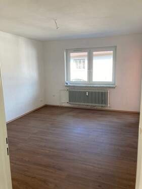 Wohnzimmer mit weiß angelegten Wänden, braunem Vinyl-Designboden in Holzoptik und Zugang zum Balkon - 