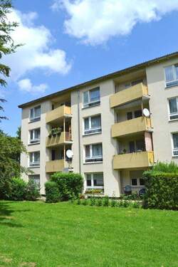 Rückansicht eines mehrstöckigen Wohngebäudes mit Balkonen, umgeben von Bäumen und grünen Sträuchern - 3 Zimmer Etagenwohnung zur Miete in Kassel