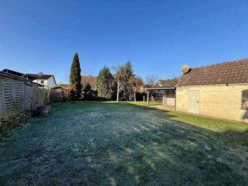 Blick in den Garten und auf das Garagengebäude mit angeschlossenem überdachten Sitzplatz - 