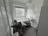 Blick in Bad mit weißen Wandfliesen, weißem Waschbecken, grauen Bodenfliesen, Hänge-WC und Badewanne mit Duschvorrichtung und Fenster - 3 Zimmer Etagenwohnung in Meerbusch