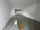 Blick in Wohnzimmer mit grauem PVC-Boden in Laminatoptik und weißen Wänden mit weißen Fenstern und zwei weißen Zimmertüren - 