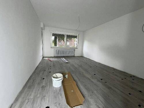 Blick in Wohnzimmer mit grauem PVC-Boden in Laminatoptik und weißen Wänden mit weißen Fenstern und zwei weißen Zimmertüren - 