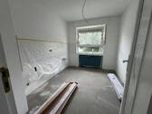 Blick von Diele in Küche mit weißen Fliesenspiegel und tapezierfähigen Wänden, weißen Fenstern und grauem Boden - 