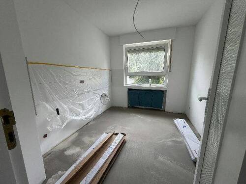 Blick von Diele in Küche mit weißen Fliesenspiegel und tapezierfähigen Wänden, weißen Fenstern und grauem Boden - 