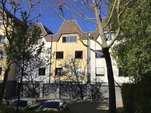 Rückansicht eines mehrstöckigen Wohngebäudes mit Garagen und Stellplätzen, umgeben von Bäumen und grünen Hecken. - 3 Zimmer Etagenwohnung zur Miete in Frankfurt am Main