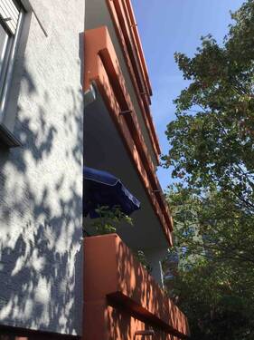 Rückansicht des mehrstöckigen Wohngebäudes mit Balkonen, umgeben von Grünanlagen mit Bäumen und grünen Sträuchern - Schöne SINGLEWOHNUNG sucht Nachmieter!