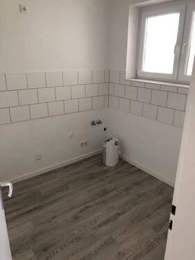 Blick von Diele in Küche mit weißen Fliesenspiegel, grauem PVC -Boden und tapezierfähigen Wänden mit weißen Fenstern - 2 Zimmer Etagenwohnung in Neuss