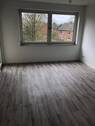 Blick von Diele in Wohnzimmer mit grauen PVC-Boden und tapezierfähigen Wänden mit weißen Fenstern und Tür zu Balkon - Etagenwohnung mit 51,30 m&sup2; in Neuss zur Miete