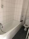 Blick in Bad mit weißen Wandfliesen, grauen Bodenfliesen WC und Badewanne - 