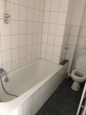 Blick in Bad mit weißen Wandfliesen, grauen Bodenfliesen WC und Badewanne - 