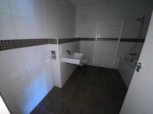 Blick in Bad mit weißen Wandfliesen, braunen Bodenfliesen Hänge-WC - 
