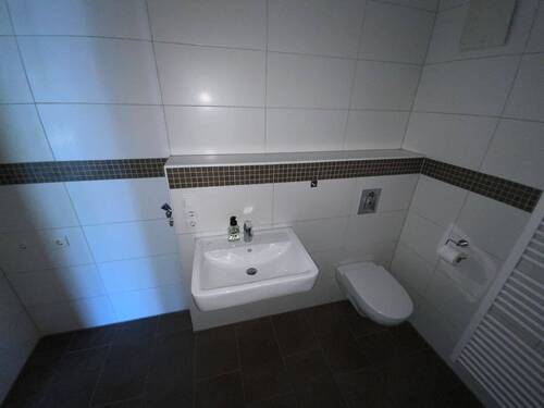 Blick in Bad mit weißen Wandfliesen und Wachbecken - 
