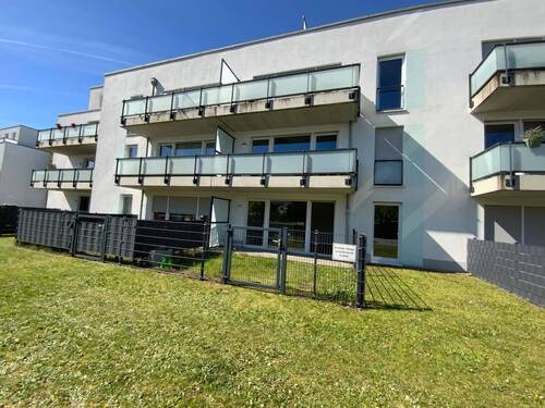  Blick auf Terrasse mit grauem Betonboden und grauer Zaun aus Metall mit Glasscheiben und Blick auf den Rasen die Außenanlage - 