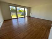 Blick von in Wohnraum mit braunem PVC-Boden und weißen Wänden mit weißen ebenerdigen Fenstern und weißer Terrassentür, Garten und Zaun - 