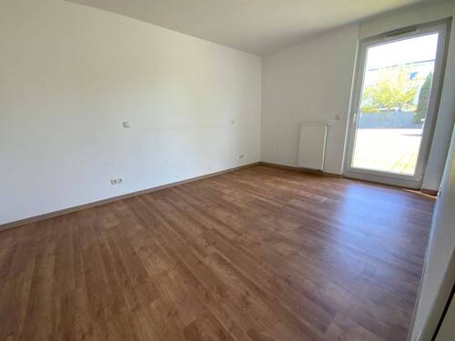 Blick von Diele in Schlafraum mit braunem PVC-Boden und weißen Wänden mit weißen ebenerdigen Fenstern - 