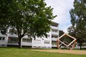 Akazienallee 12, Außenansicht mit Blick über Spielplatz mit Kletterwürfel auf Balkonseite - 4 Zimmer Etagenwohnung in Baunatal