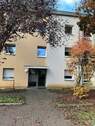Eingangsbereich des mehrstöckigen Wohnhauses umgeben von Grünanlagen mit Bäumen - Gemütliche, kleine 2-Zimmerwohnung sucht neue Mieter!