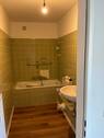 Bad mit grünen Wandfliesen und Fußbodenbelag in Holzoptik - 1 Zimmer Etagenwohnung in Wiesbaden