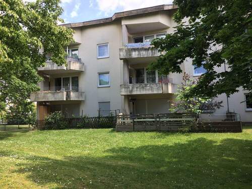 Gebäude Rückseite des mehrstöckigen Wohnhauses mit Blick in die Grünanlage mit Sträuchern - Tolle 2-Zimmerwohnung im Erdgeschoß sucht neue Mieter!