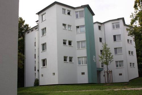 Seitenansicht eines mehrstöckigen Wohngebäudes mit Balkonen, umgeben von Bäumen und grünen Sträuchern - Schicke-3-Zimmer-Wohnung - 531,00&nbsp;EUR Kaltmiete, ca.&nbsp; 66,00&nbsp;m&sup2;&nbsp;Wohnfl&auml;che