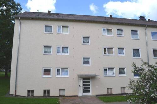 .Vorderansicht eines mehrstöckigen Wohngebäudes , umgeben von Bäumen und grünen Sträuchern - Schicke 3-Zimmer-Wohnung - 490,00 EUR Kaltmiete, ca.  65,60 m² Wohnfläche