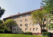Hausansicht eines Mehrfamilienhauses umgeben von grüner Wiese und Bäumen. - Moderne 2-Zimmer-Wohnung mit Balkon zu vermieten!