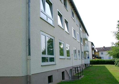 Rückansicht auf das Mehrfamilienhaus mit einer Rasenfläche und großen Fenstern - Schöne 2-Zimmer Wohnung mit neuen Bodenbelägen und Balkon zu vermieten