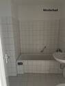 Musterbad mit Badewanne, weißen Sanitärobjekten, hellen Wand- und Bodenfliesen und Waschmaschinenanschluss - 