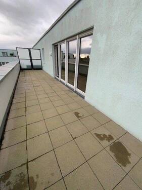 Blick auf Terrasse mit grauem Betonboden und grauer Balkonbrüstung aus Metall mit Glasscheiben und Blick auf die Außenanlage - 