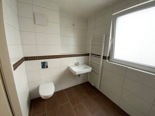 Blick in Bad mit weißen Wandfliesen, braunen Bodenfliesen Hänge-WC und bodengleiche Dusche - 2 Zimmer Etagenwohnung in Meerbusch