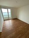 Blick von Diele in Schlafraum mit braunem PVC-Boden und weißen Wänden mit weißen ebenerdigen Fenstern - 