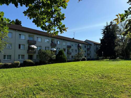 Rückansicht des mehrstöckigen Wohngebäudes umgeben von Grünanlagen mit Bäumen und Sträuchern - 