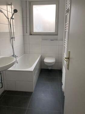 Modernisiertes Badezimmer mit Fenster und Badewanne. Dunkler Fliesenboden und hell geflieste Wände.jpeg - 