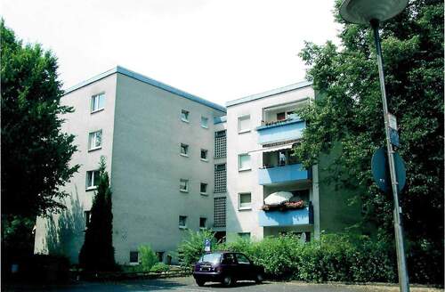An der Bauna 10, Außenansicht auf den Eingangsbereich eines mehrgeschossigen Wohngebäudes mit heller Fassade, farbig abegesetzten Balkonbrüstungen und Flachdach..JPG - 4 Zimmer Etagenwohnung zur Miete in Baunatal