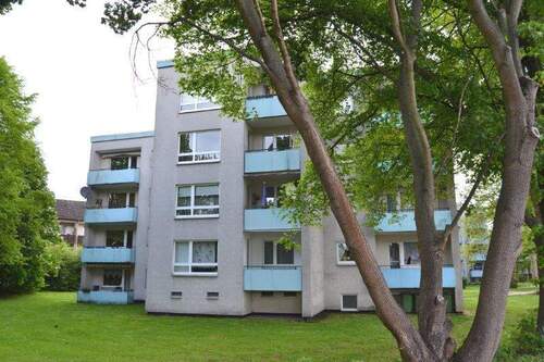 Am Mühlenacker 8, Außenansicht über die Grünanlage mit altem Baumbestand auf ein freistehendes mehrgeschossiges Wohngebäude mit heller Fassade, farblich abgesetzten Balkonen und Flachdach - 4 Zimmer Etagenwohnung zur Miete in Baunatal