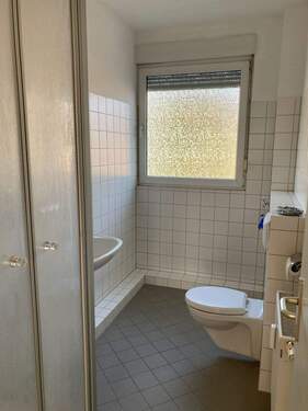 Bad mit Fenster und Dusche und weißen Wandfliesen sowie grauen Bodenfliesen - 2 Zimmer Etagenwohnung zur Miete in Friedrichsdorf