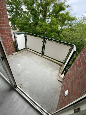 Blick von Wohnzimmer auf Balkon mit grauem Betonboden und Blick auf Rasen der Außenanlage - 