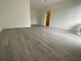 Blick in Wohnzimmer mit grauem PVC-Boden in Laminatoptik und weißen Wänden - 