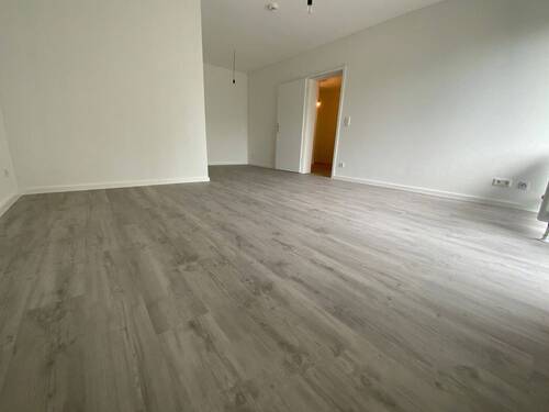Blick in Wohnzimmer mit grauem PVC-Boden in Laminatoptik und weißen Wänden - 