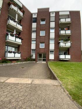 Blick auf den Hauseingang des braun verziegelten Hauses mit weißer Glaseingangstür und Wohnungsfenster - 160047204125 'Gemütliche 2-Zimmer-Wohnung in Meerbusch Büderich-RheinEck - 3. Stock'