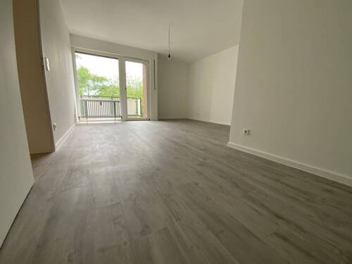 Blick in Wohnzimmer mit grauem PVC-Boden in Laminatoptik und weißen Wänden mit weißen Fenstern und weißer Balkontür - Etagenwohnung mit 57,80 m&sup2; in Meerbusch zur Miete